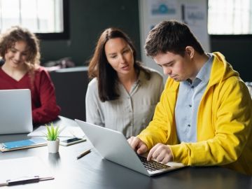 A young man working on a laptop as a female instructor guides him