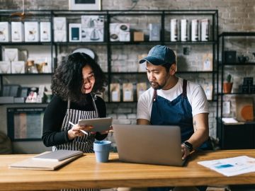 Two cafe owners complete admin work on a computer in their store