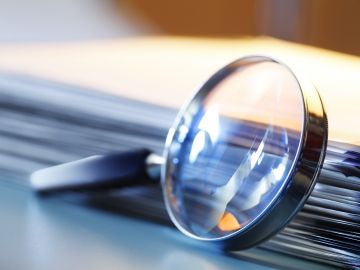 A magnifying glass rests against a stack of papers