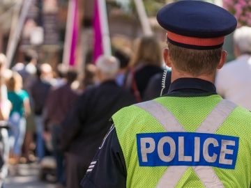 A police officer with their back turned faces a group of people walking around.