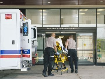 Paramedics wheel a stretcher out of a ambulance in front of a hospital.