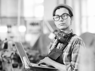 A young worker holding a laptop looks into the distance.