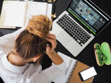 An overhead shot of a woman holding her head in front of a laptop