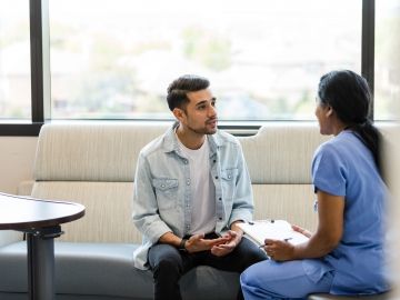 A man speaks with a female doctor in scrubs who holds a clipboard