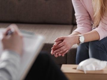 Close-up of two pairs of hands, belong to a counsellor and a patient sitting on a couch