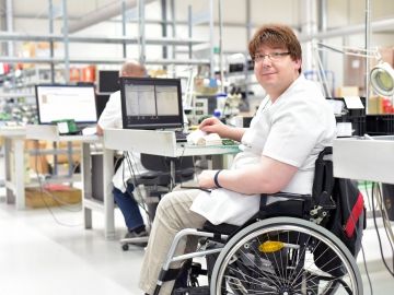 A computer technician who uses a wheelchair works at his station