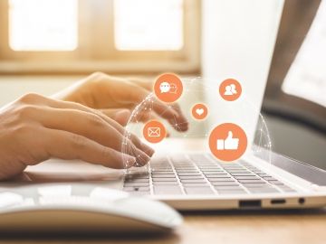 A close-up of a pair of hands typing at a laptop, with email and social media symbols superimposed