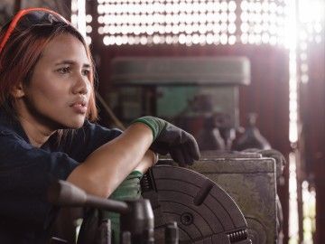 female factory worker sitting on floor with tools, looking worried about what to do