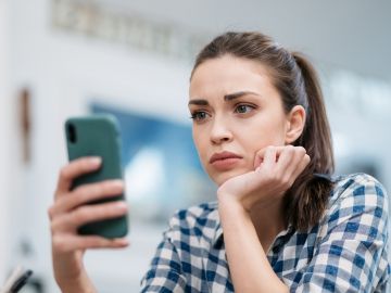 A young woman looks at her phone in frustration and exasperation