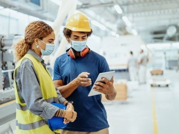 Two workers wearing masks look at a tablet together