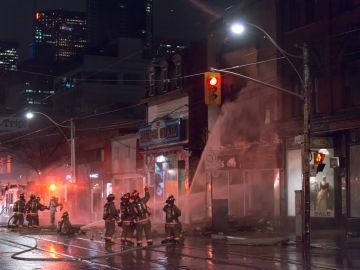 A group of firefighters aim a firehose at a building