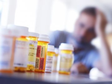 A man with his head in his hand looks at a row of empty pill bottles