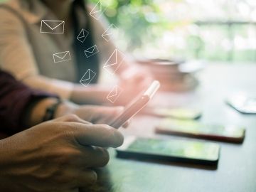 A close up of smart phones on a surface or held in people's hands, with email icons floating above them  