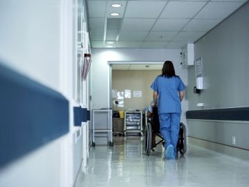 A long-term care worker pushes a resident in a wheelchair down the hall