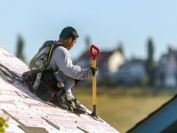 A worker sits on top of the roof of a residential new build