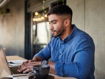 A man in a blue shirt works at a laptop on a long table