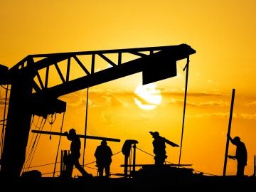 Silhouettes of construction workers against an orange sky