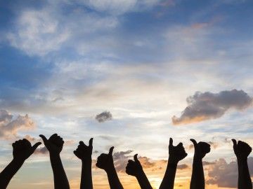 Silhouette of a row of hands holding their thumbs up against a dusky sky