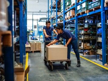 A man and a woman work together to push a trolley through a warehouse