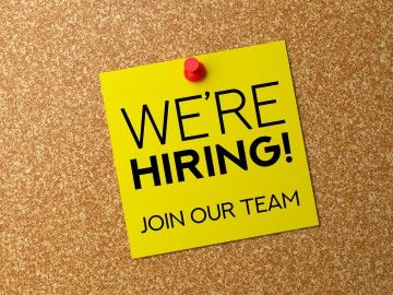 A yellow note tacked on a cork board reads: "we're hiring! join our team"
