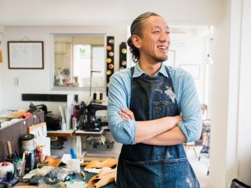 Japanese craftsperson stands in front of his workstation, smiling