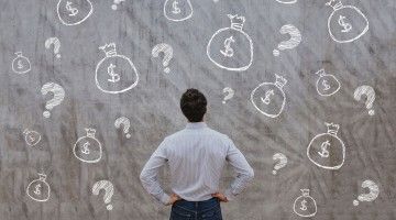 A man looks at a blackboard with chalk written money symbols and question marks