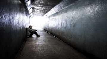 A homeless young man sits on the ground, in a tunnel