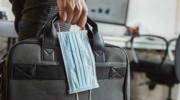 Close-up of a hand holding a surgical mask and a laptop case