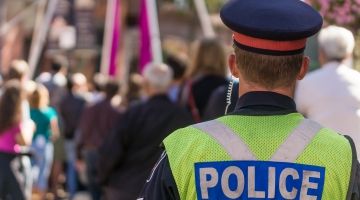 A police officer with their back turned faces a group of people walking around.