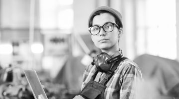 A young worker holding a laptop looks into the distance.