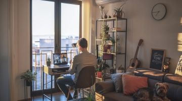 A man sits at a desk on a video call in his apartment's living room.