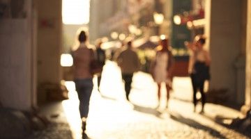 A blurry image of figures walking along a sunlit street