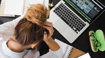 An overhead shot of a woman holding her head in front of a laptop