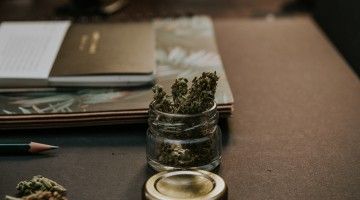 A jar of cannabis buds on a brown desk