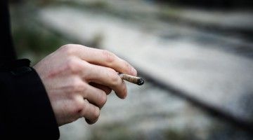 A close-up of a man's hand, holding a joint
