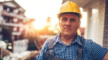 An older construction worker in a hard hat looks at the camera