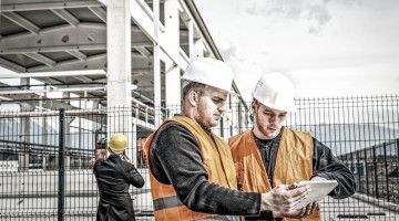 Two workers look over document at a large construction site