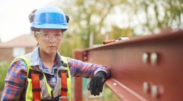 A female construction worker stands next to a steel girder