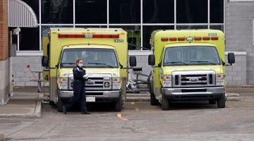 A paramedic wearing a face mask stands next to two ambulances