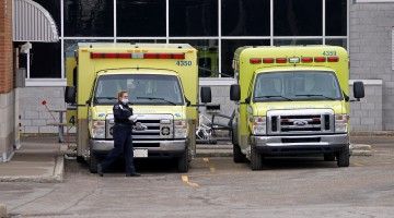 A paramedic wearing a face mask stands next to two ambulances 