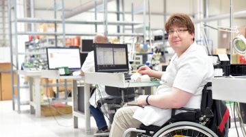 A computer technician who uses a wheelchair works at his station