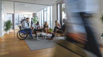 A worker in a wheelchair sits with colleagues in a busy office