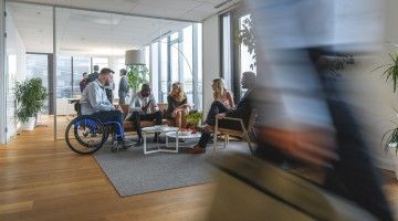 A worker in a wheelchair sits with colleagues in a busy office 