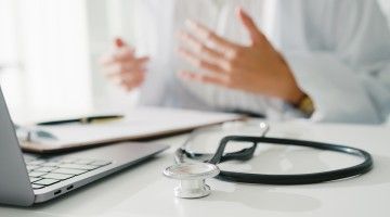 An out-of-frame doctor talks to someone on a laptop screen