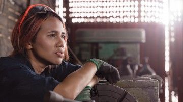 female factory worker sitting on floor with tools, looking worried about what to do