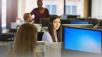 A group of customer service workers sit in front of their computers in an open office complex