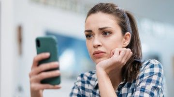 A young woman looks at her phone in frustration and exasperation