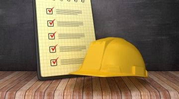 A hard hat, placed next to a check list, against a black background