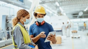 Two workers wearing masks look at a tablet together