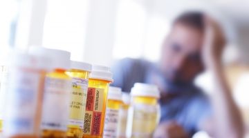 A man with his head in his hand looks at a row of empty pill bottles